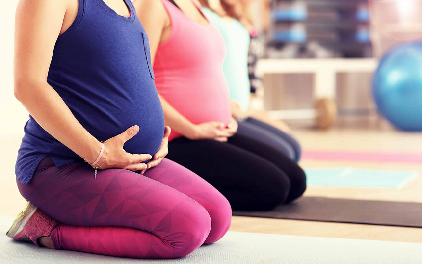 Frauen sitzen nebeneinander in einem Geburtsvorbereitungskurs und halten ihren Babybauch